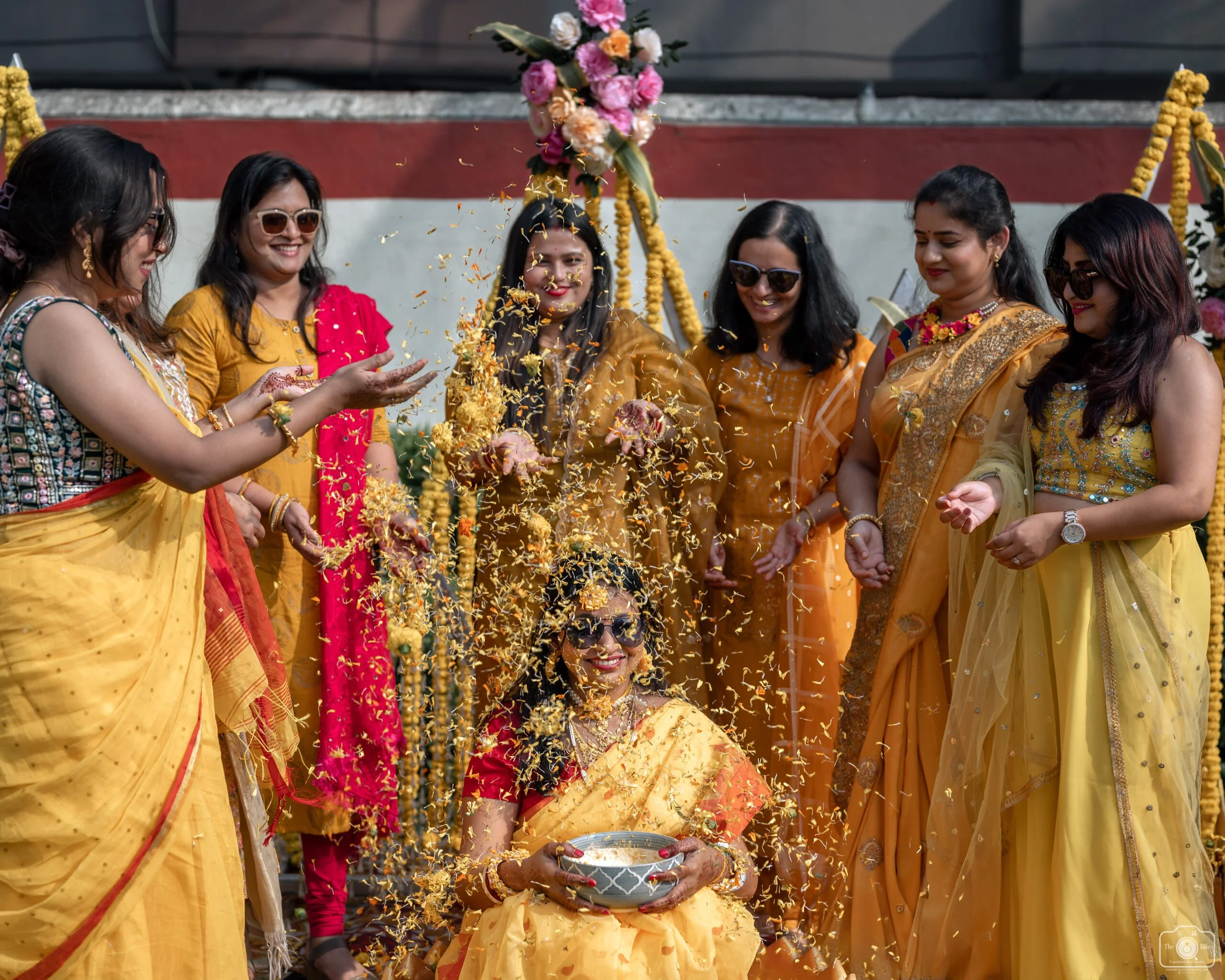 Bridesmaids are showering the bride with flower petals during the haldi ceremony